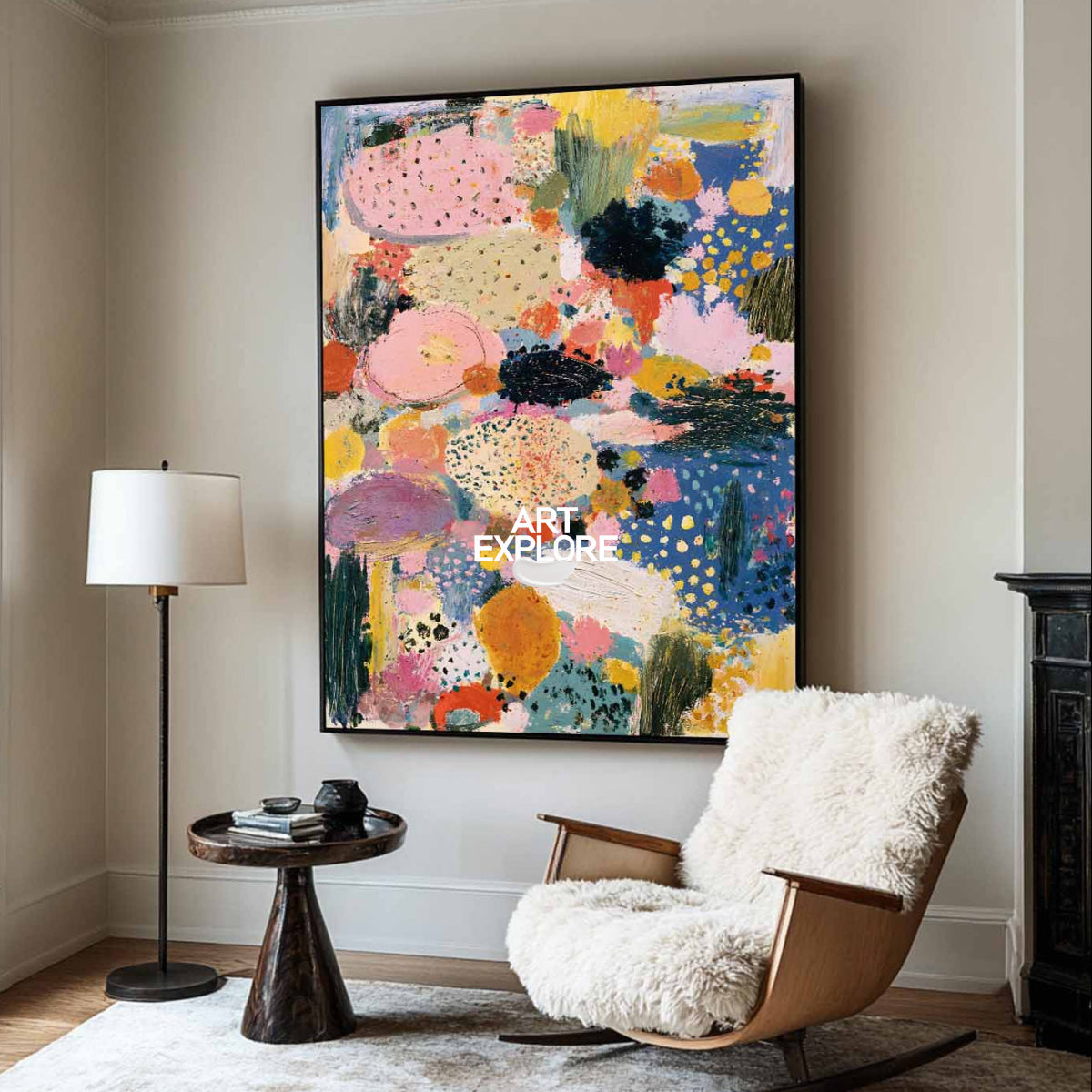 A large abstract canvas painting with vibrant pink, blue, yellow, and black brushstrokes hangs on a beige wall in a styled living room with a wooden rocking chair, white sheepskin cushion, and a floor lamp.