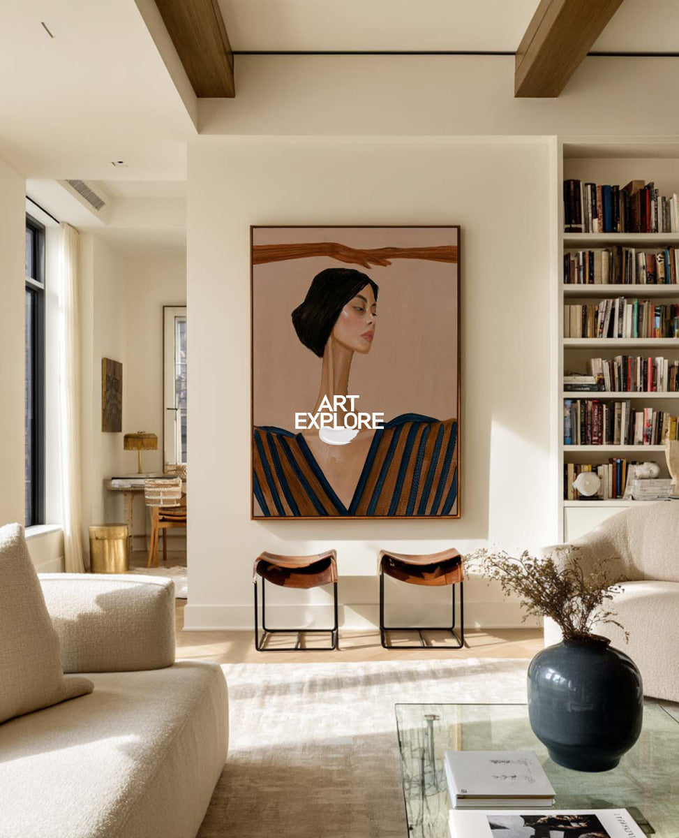 A framed art print depicting a stylized portrait of a woman with a dark head covering and blue striped clothing, hanging on a cream wall in a modern, sunlit living room with bookshelves and a sofa.