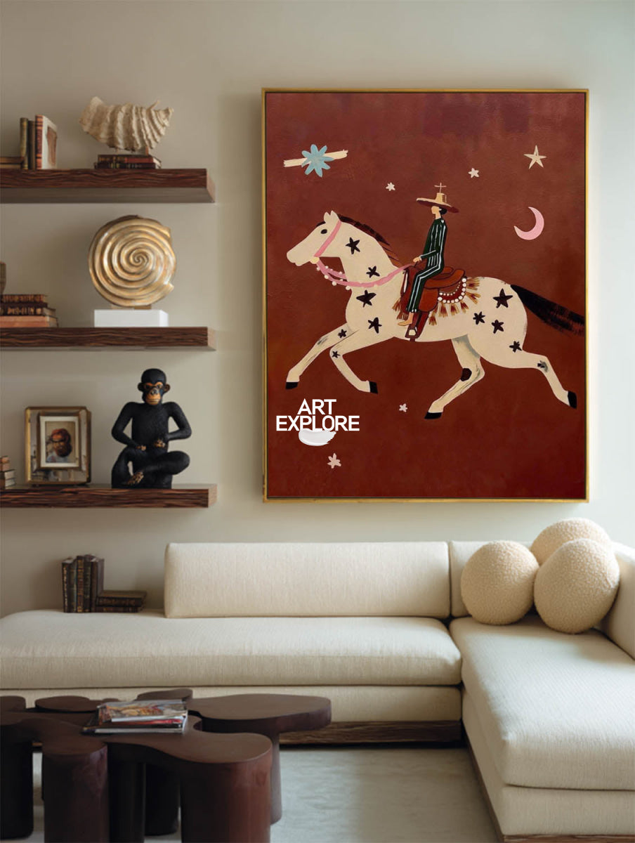 A framed art print depicting a cowboy riding a star-spangled horse against a reddish-brown background, hanging on a beige wall in a modern living room setting above a cream-colored sectional sofa.