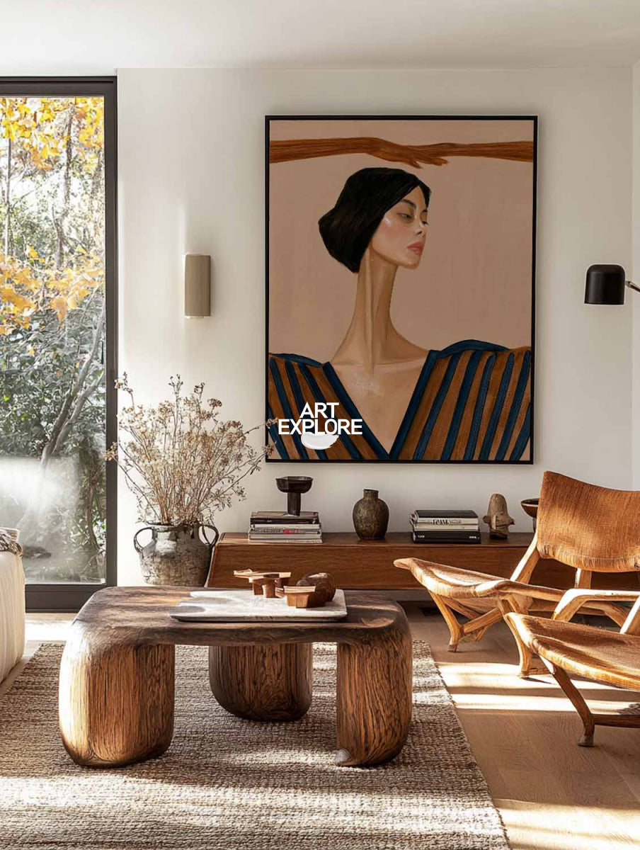 A large framed art print featuring a stylized portrait of a woman with dark hair and a blue-and-brown striped top, displayed on a white wall in a modern living room with a wooden coffee table, chair, and window view.