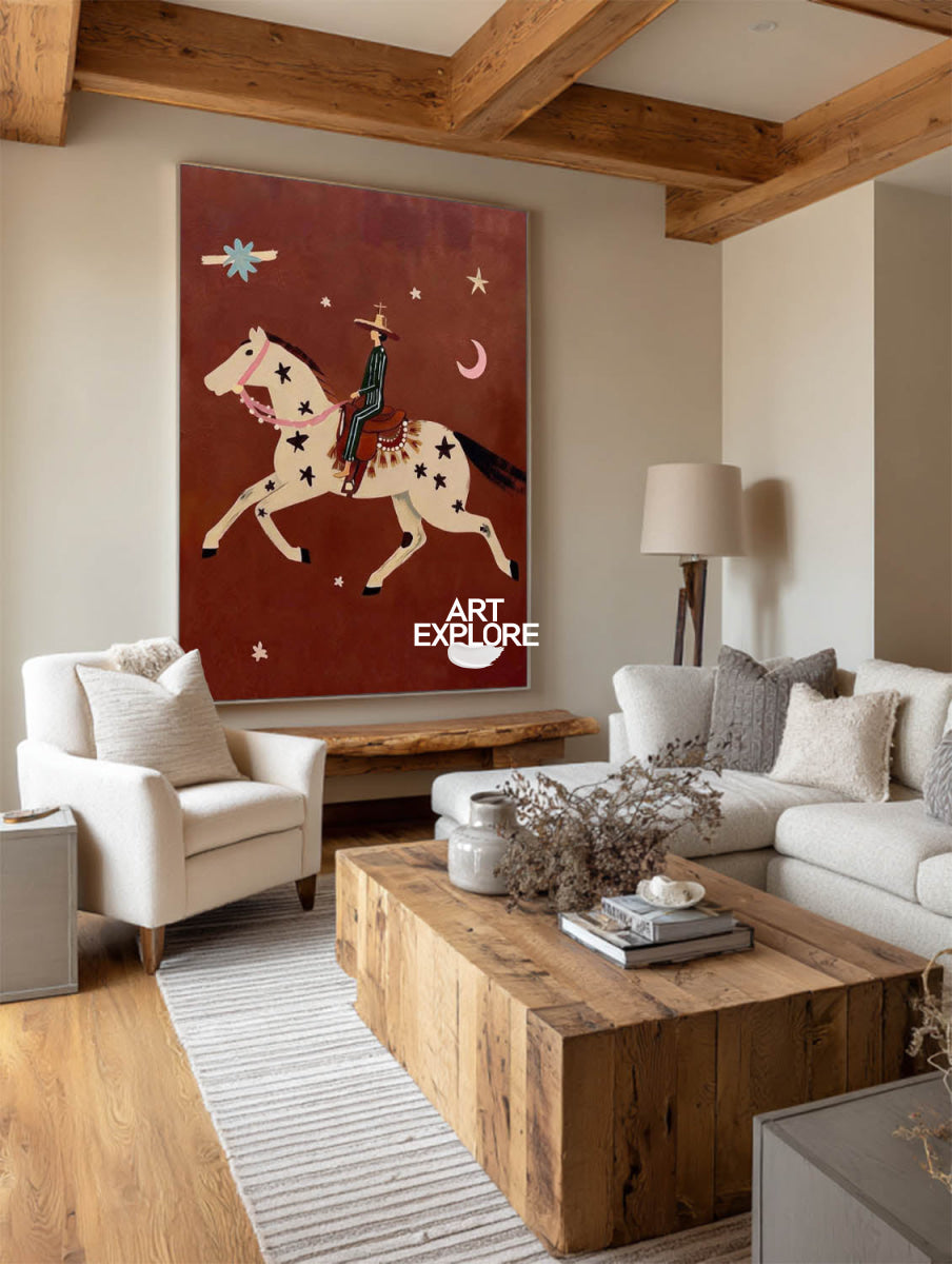 A large vertical canvas print featuring a whimsical western-style painting of a cowboy riding a white horse under a red starry sky, displayed on a beige wall in a modern living room with a wooden coffee table, white sofa, and exposed wood ceiling beams.
