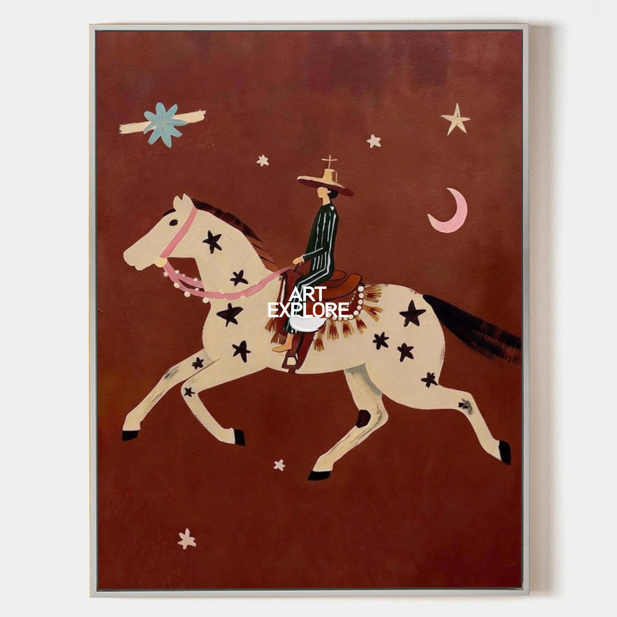 A framed art print featuring a stylized cowboy riding a horse against a dark reddish-brown background, with stars, a crescent moon, and abstract shapes. The print is housed in a thin light gray frame and is photographed against a plain white wall.