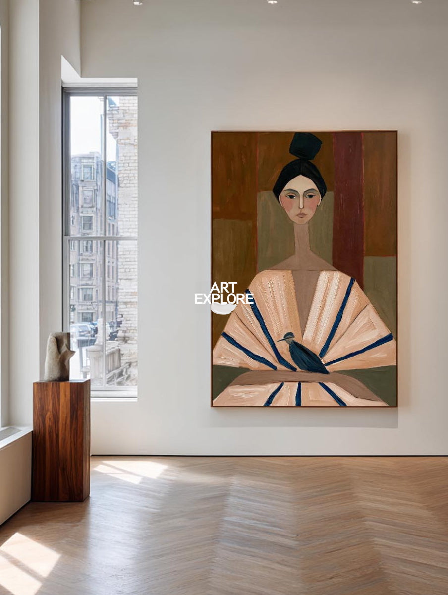 A large framed art print depicting a stylized woman in a fan-like garment with a bird, displayed on a white gallery wall in a bright modern room with wood floors and windows.