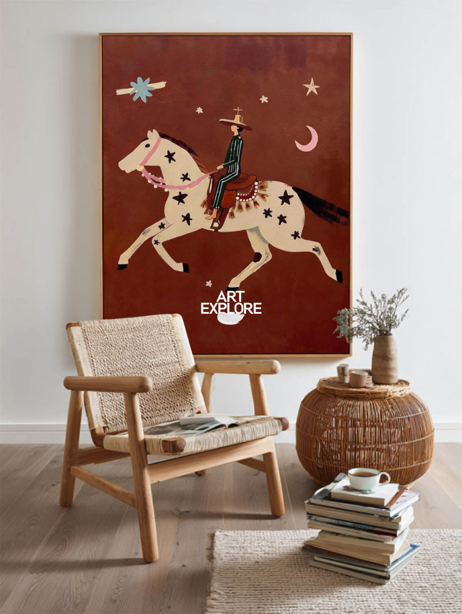A large framed wall art print featuring a stylized cowboy riding a horse against a rust-brown background, displayed in a modern living room setting above a woven armchair and next to a wicker side table.